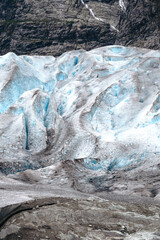 Detailed view of blue glacier ice showing deep crevasses and textured surfaces against a steep rocky mountain wall in an alpine outdoor environment. © JULIA