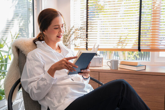 Asian woman in casual clothes, reading a book while sitting on c