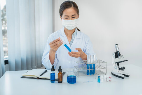 Scientist woman in protective face mask to shaking blue liquid i