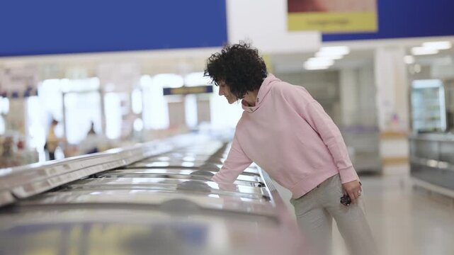 A woman in a pink hoodie is shopping in a grocery store. She is looking at the refrigerated section