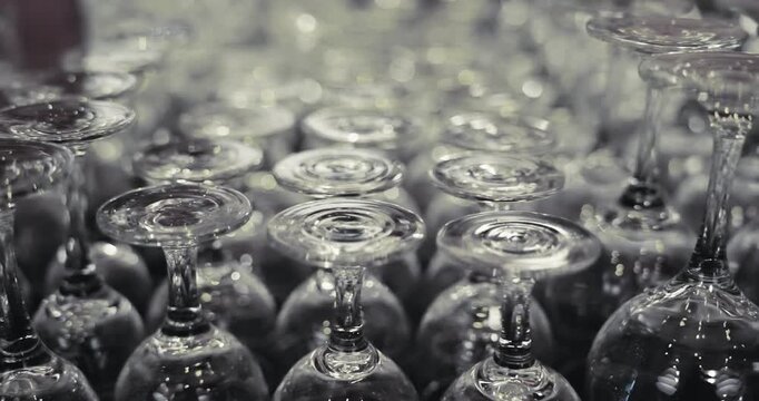 A bunch of wine glasses are lined up on a table in bar, hotel. The glasses are all clear and empty