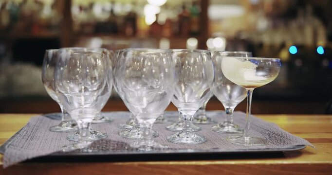 A table with a tray of glasses on bar counter. The glasses are all clear and empty. The table is wooden and has a brown color