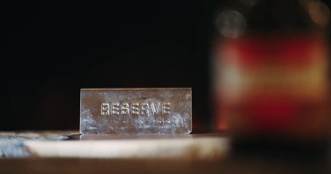 A metal sign with the word "Reserve" written on it sits on a wooden table in hotel with fire burning fireplace at background