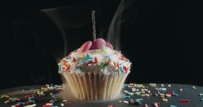 A cupcake with a lit candle on top and sprinkles on the bottom
