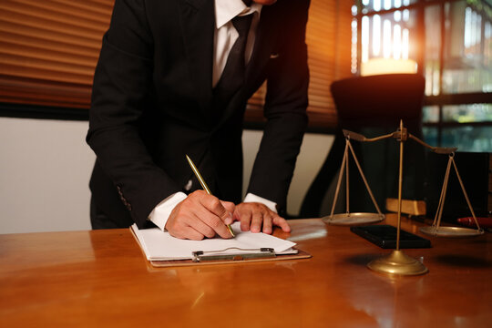 Lawyer Standing and Signing Legal Document at Desk with Scales of Justice