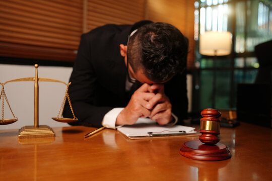 Stressed Asian Lawyer Resting Head on Hands at Law Office Desk