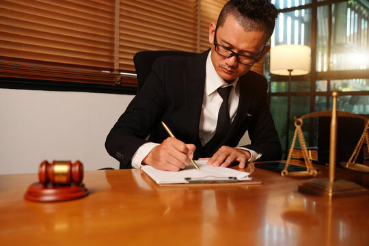 Asian Lawyer Writing on Contract Document in Legal Office Environment