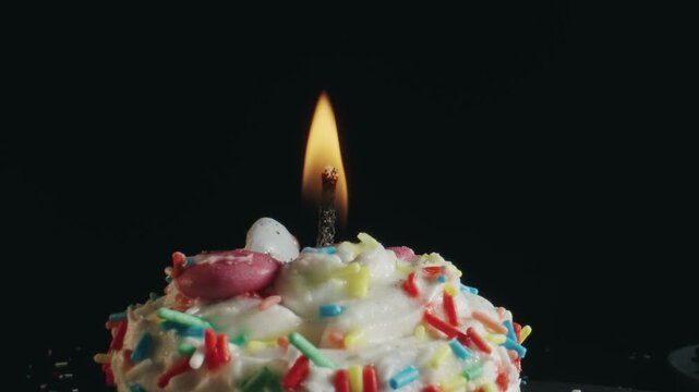 A lit candle on top of a cupcake with sprinkles
