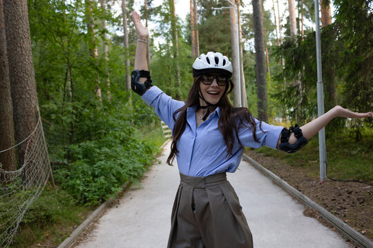 Happy woman in a helmet on rollerblades spreads her arms on a forest path, freedom and joy concept