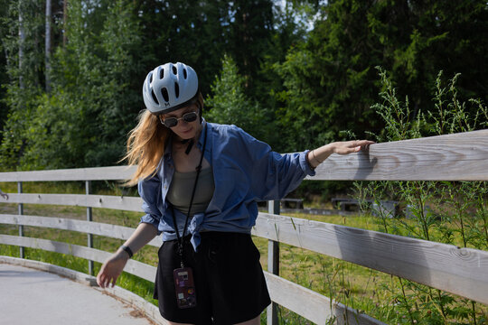 Beginner woman on rollerblades holding a wooden fence and looking down at her skates