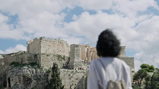 Tourist curly hair woman enjoy the panoramic view of Acropolis in Athens on sunny day from Areopagus Hill
