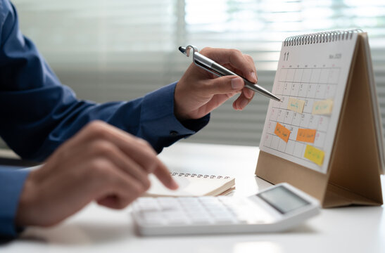 Business professional using a calculator and desk calendar to plan payments, deadlines, budgets and financial schedules, representing organized money management and monthly expense planning.