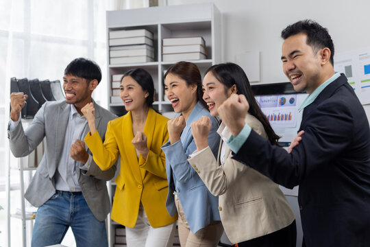 Euphoric business team celebrating success in office. Diverse business team in an office cheering, happily raising their fists, celebrating achievement and victory together.