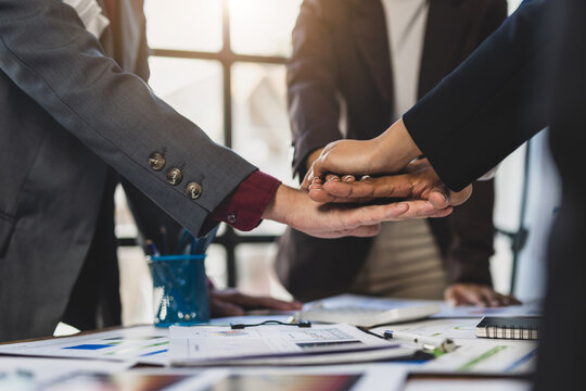 Business team members stacking diverse hands over financial graphs, showing unity and collaboration during a data analysis meeting.