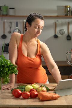 Woman in Orange Top Using Digital Tablet In Contemporary Kitchen With Fresh Vegetables