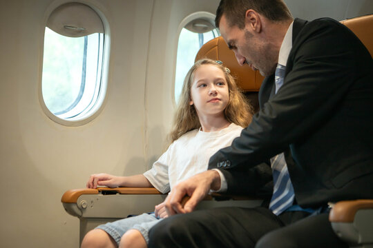 Businessman traveling with his daughter inside a commercial airplane cabin, representing family travel and business mobility
