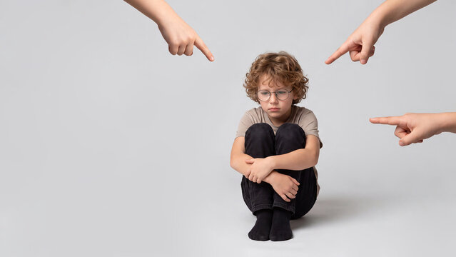 Sad boy surrounded by children's hands point at him from different directions. Minimal concept of peer pressure, social isolation, bullying, vulnerability and emotional distress.