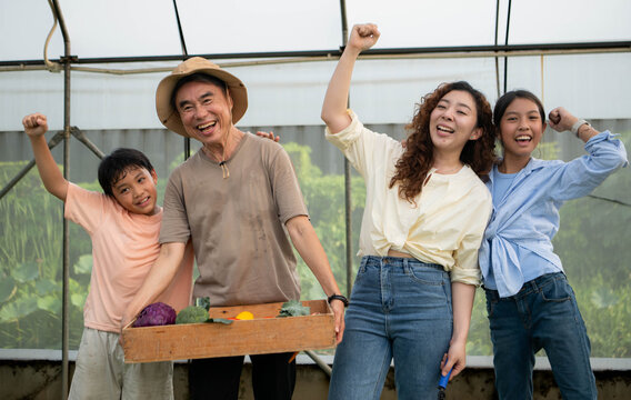 Joyful family celebrating a successful vegetable harvest together inside a greenhouse,