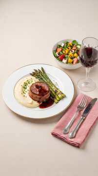 Filet mignon medallion with bacon, mashed potatoes, grilled asparagus, salad, and a glass of red wine