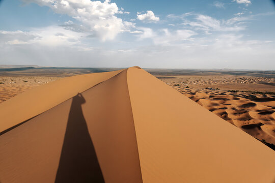 Long shadow of a person appearing on a desert sand dune with erg chebbi, merzouga, and the sahara in the background