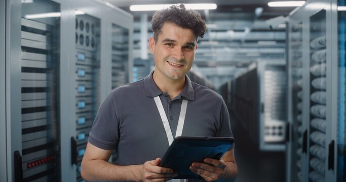 In Modern Data Center, IT Specialist Operates Digital Tablet in Server Room Corridor. Mobile Cloud Management and System Diagnostics Ensure Seamless Server Infrastructure Operation. Portrait.