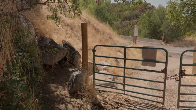 Still shot of a metal gate beside a dirt trail on a dry hillside.