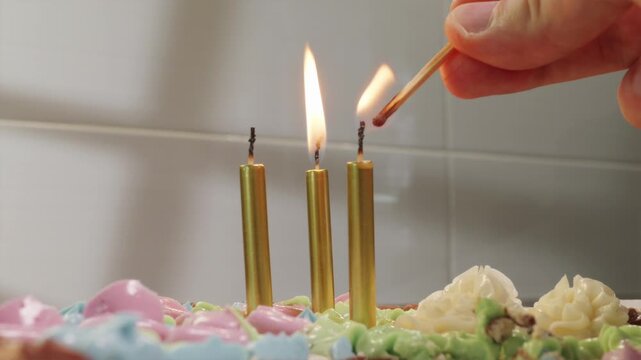 POV shot lighting candles on birthday cake against bright white kitchen background