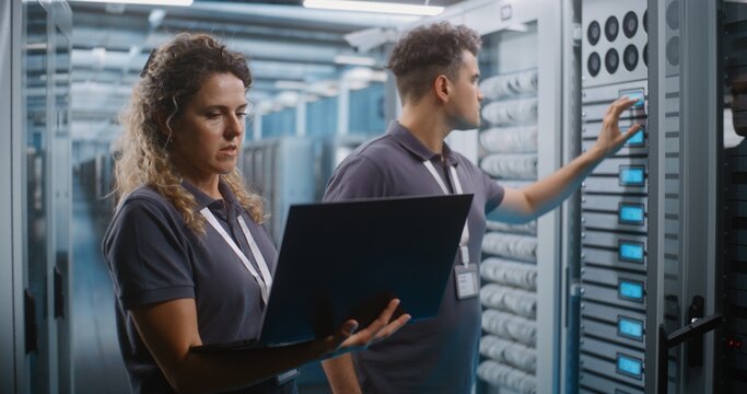 Female IT Specialist and Male Colleague Review System Diagnostics on Laptop Together in Data Center Server Room. Teamwork, Cloud Infrastructure Management Ensure High Availability Server Operations.
