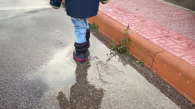 A little boy walks through puddles in rubber boots after the rain. 4k, slow motion.