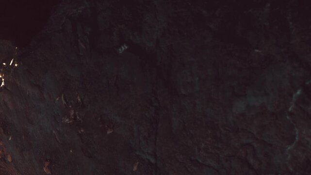 Faint light filters through a caves entrance, revealing rough, textured stones. Shadows creep along the walls, creating an enchanting atmosphere in this mysterious underground world.