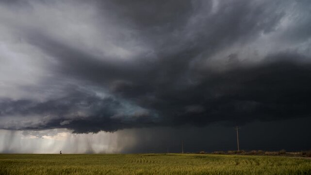 Dramatic timelapse captures massive storm cell clouds rolling over golden cornfields in the USA plains, with intense lighting, moody atmosphere, and sweeping panoramic landscape.