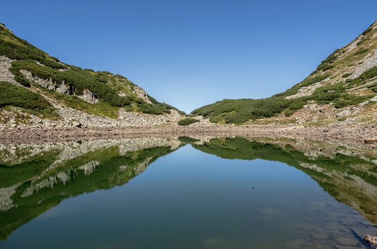 A scenic view of Mija Lake (Lacul Mija) nestled in a glacial cirque with rocky shores and alpine vegetation in the Par&acirc;ng Mountains, Romania.