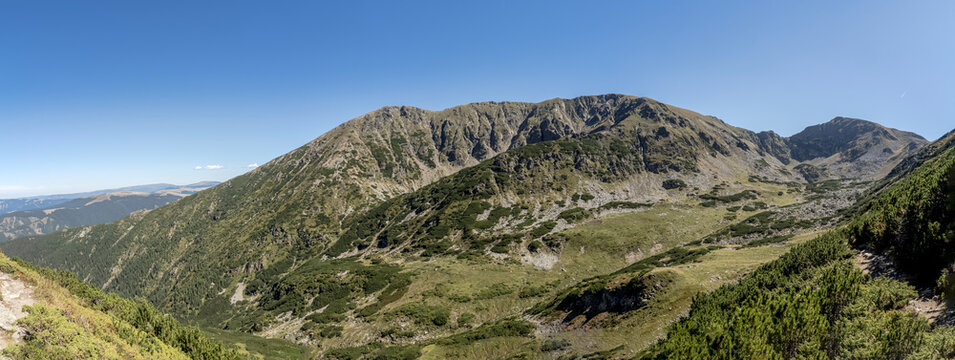 A wide panoramic view of glacial cirques and rocky mountain peaks covered with alpine vegetation in the Par&acirc;ng Mountains, Romania.
