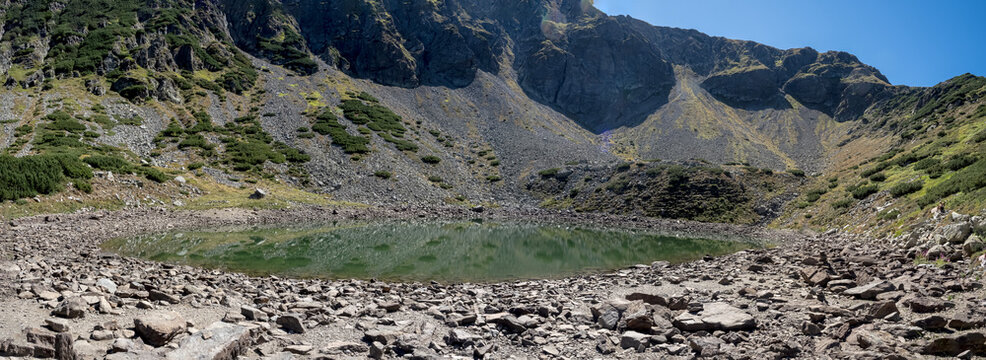 A panoramic view of Mija Lake nestled in a glacial cirque surrounded by rocky mountain slopes and alpine vegetation in the Par&acirc;ng Mountains, Romania.