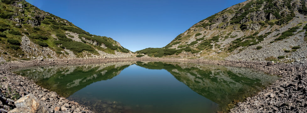 A panoramic view of Mija Lake nestled in a glacial cirque surrounded by rocky mountain slopes and alpine vegetation in the Par&acirc;ng Mountains, Romania.