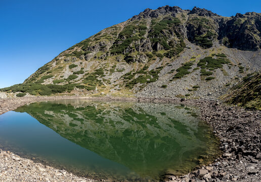 A panoramic view of Mija Lake nestled in a glacial cirque surrounded by rocky mountain slopes and alpine vegetation in the Par&acirc;ng Mountains, Romania.