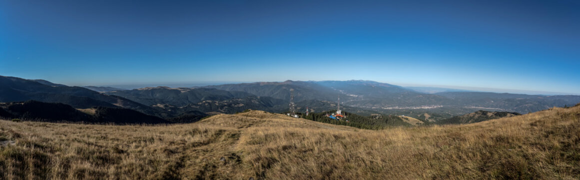 A panoramic view from the Par&acirc;ng Mountains towards the Jiu Valley, featuring alpine ridges and communication towers under a clear blue sky.