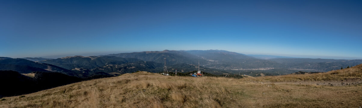 A panoramic view from the Par&acirc;ng Mountains towards the Jiu Valley, featuring alpine ridges and communication towers under a clear blue sky.