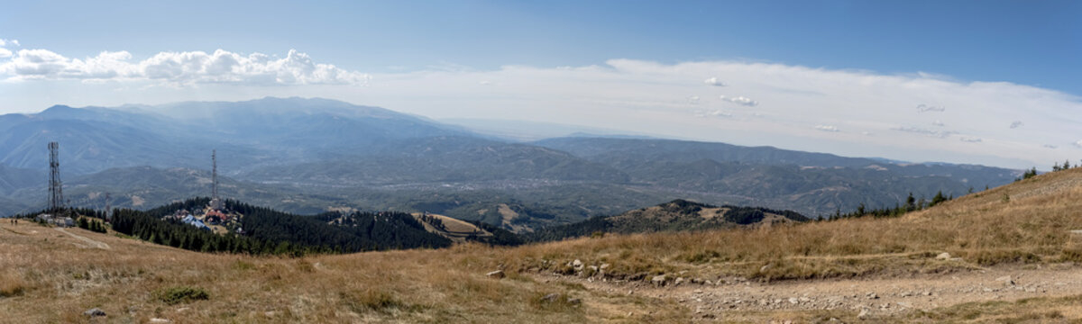 A panoramic view from the Par&acirc;ng Mountains towards the Jiul Valley, showcasing vast rolling hills, dense forests, and distant settlements under a clear blue sky.