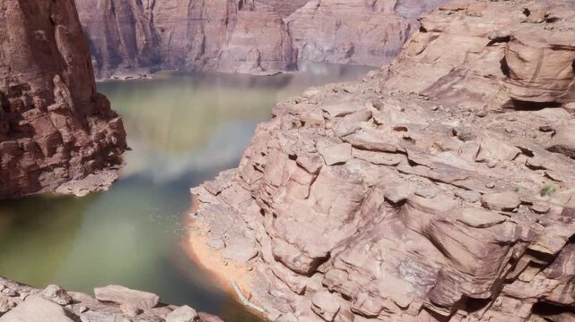 A breathtaking scene unfolds at the canyon, where rocky cliffs frame calm waters. Shades of brown and green meld as reflections dance on the surface under a clear sky.