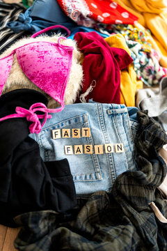 Top view pile of colorful clothing with denim and letter tiles spelling FAST FASHION, messy wardrobe concept for consumerism
