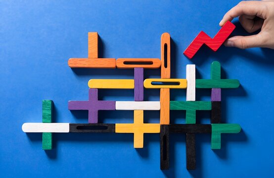 Colorful wooden puzzle pieces arranged on blue surface with hand placing red block, symbolizing logical thinking, problem solving and creativity generated ai