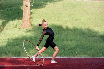 Athletic Young Girl Practicing Gymnastics with a Hoop Outdoors. Determined young girl performing artistic motions with a hoop on sunny day outdoors. © Loginova