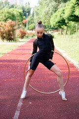 A young gymnast wearing black athletic wear performs with a hoop during practice on a track outdoors. The sport of rhythmic gymnastics blends flexibility, strength, and grace. © Loginova