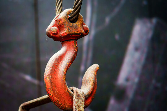 Close up shot of weathered red steel crane hook hanging on wire rope cable.