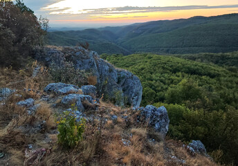 Fototapeta premium Rugged limestone rocks and dry grass on Kopus-ko overlooking the densely forested Garadna Valley at dawn in the Bukk Mountains, Hungary.