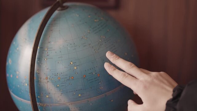 A person pointing at a globe with the words "star" on it. The globe is blue and has a white star on it