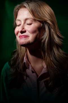 A close-up portrait of a woman smiling with her eyes closed, conveying calm joy and contentment. Natural freckles, soft lighting and relaxed expression create an intimate, candid emotional moment.