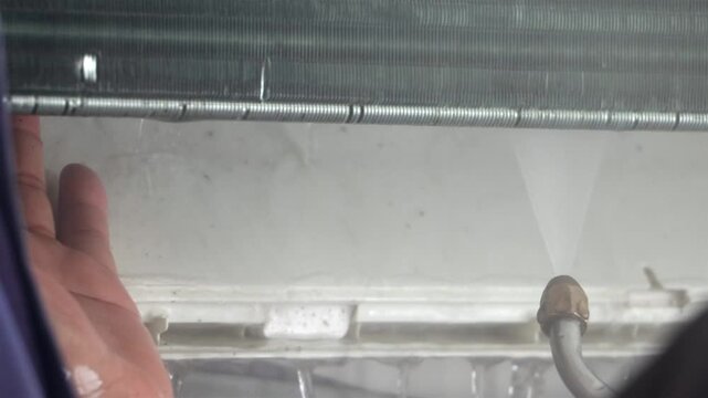 Repairman cleans air conditioner using water stream, close up.