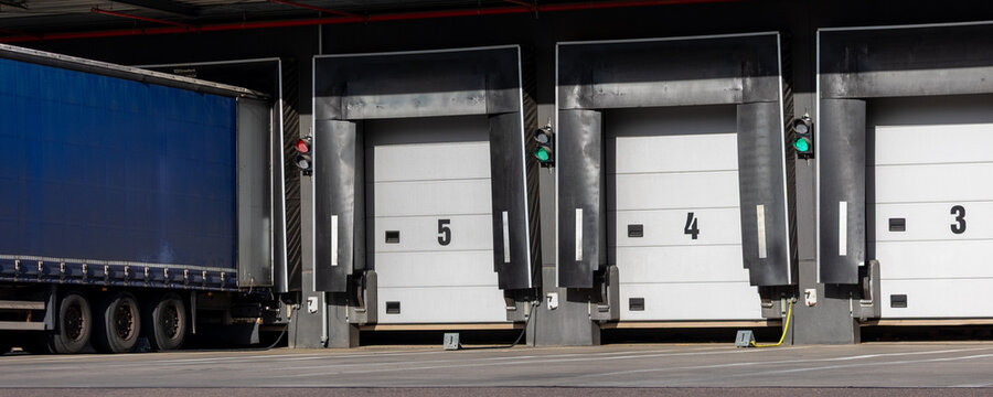 Innovative modern logistics warehouse center complex building exterior bay gate semi-trailer unloading goods distribution warm blue sunset sky background. Cargo storage facility industry building